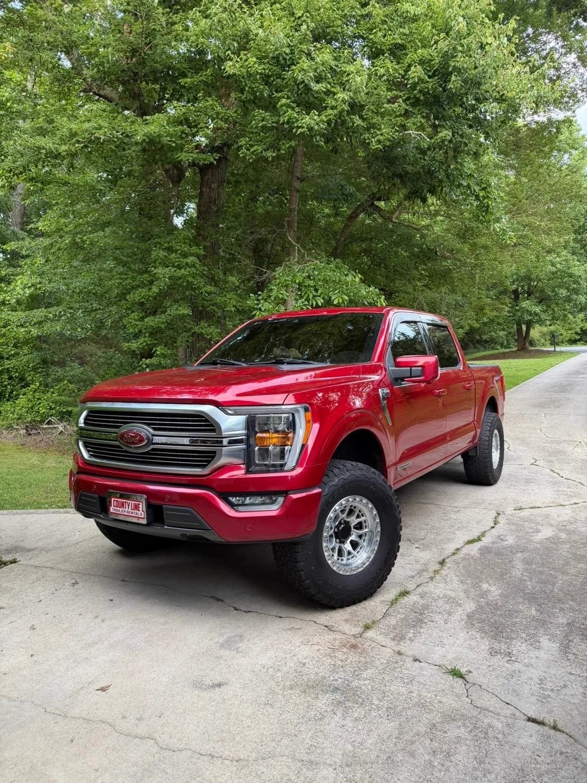 Lifted red Ford F-150 on custom wheels in a driveway