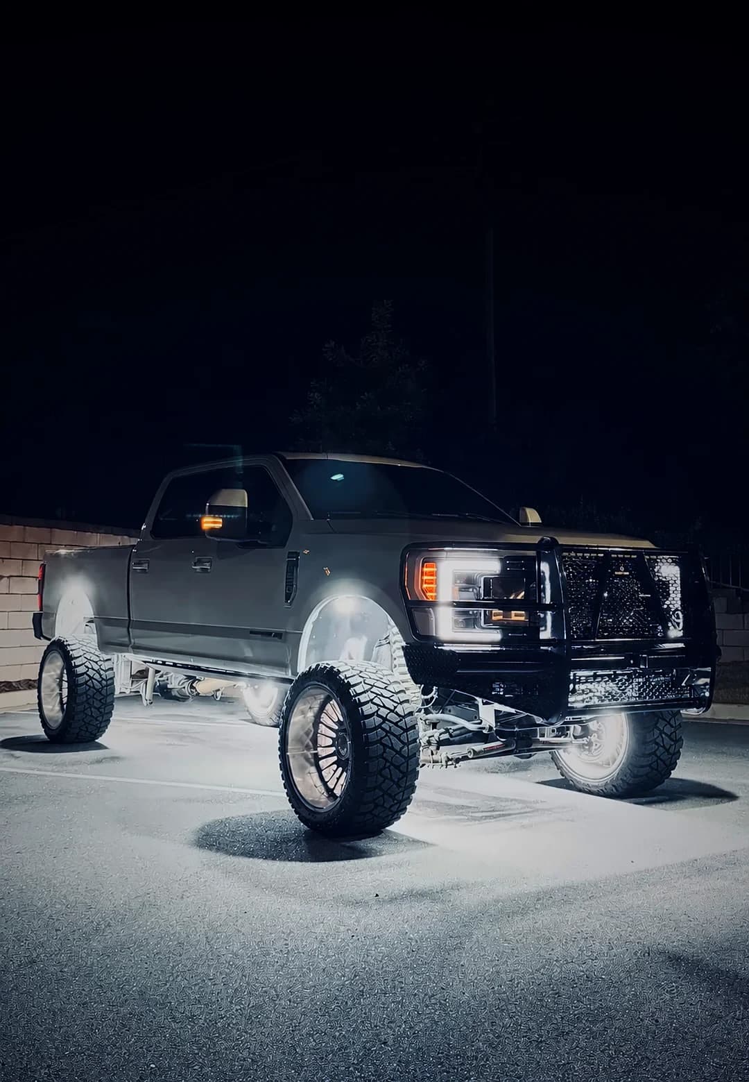 Lifted Ford F-250 at night with LED wheel lights glowing in all four wheels and rock lights lighting the ground beneath it